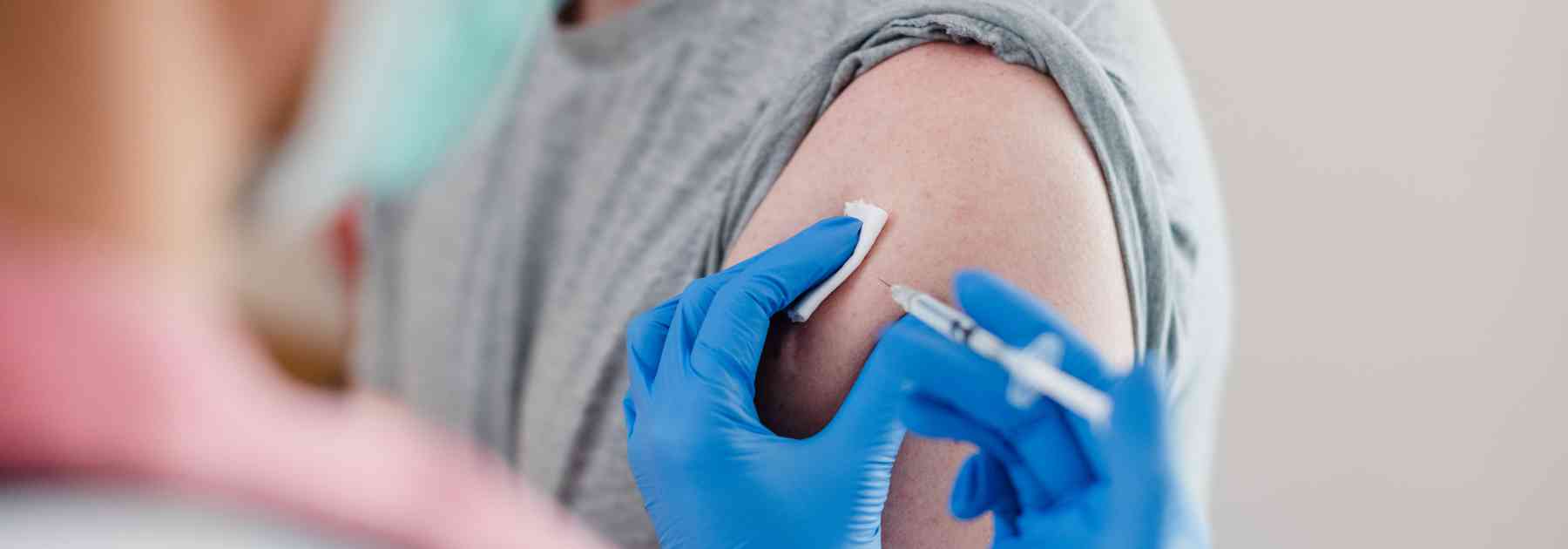 man wearing grey vest receiving vaccine in arm