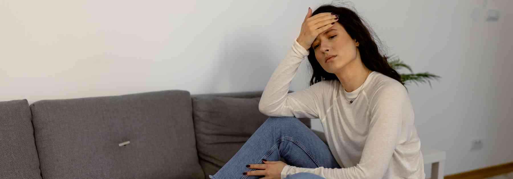 woman sitting on couch with hand on her forehead in discomfort