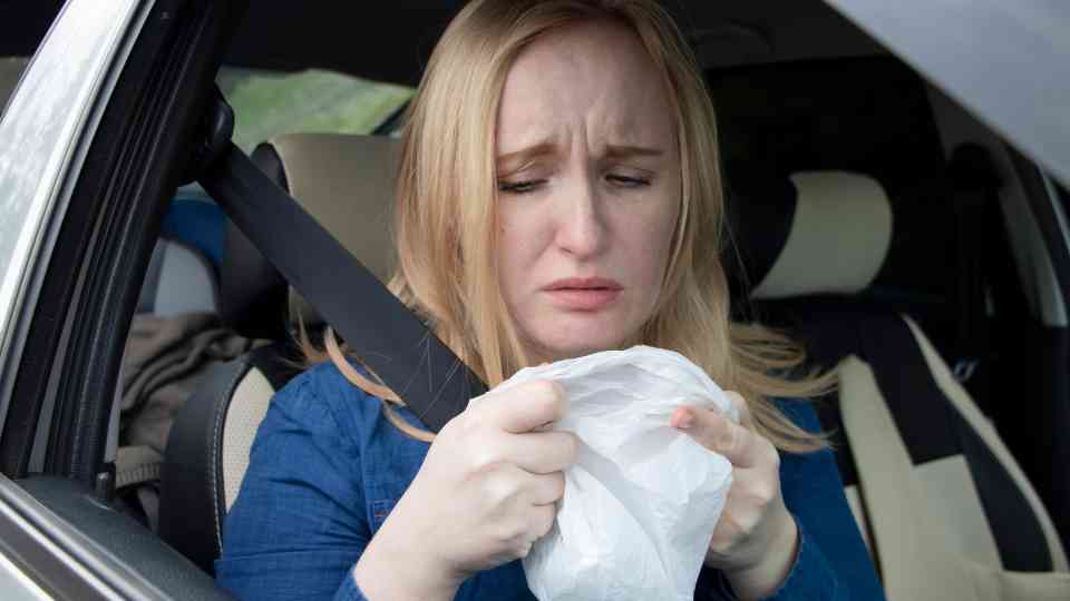woman in back seat of car holding sick bag